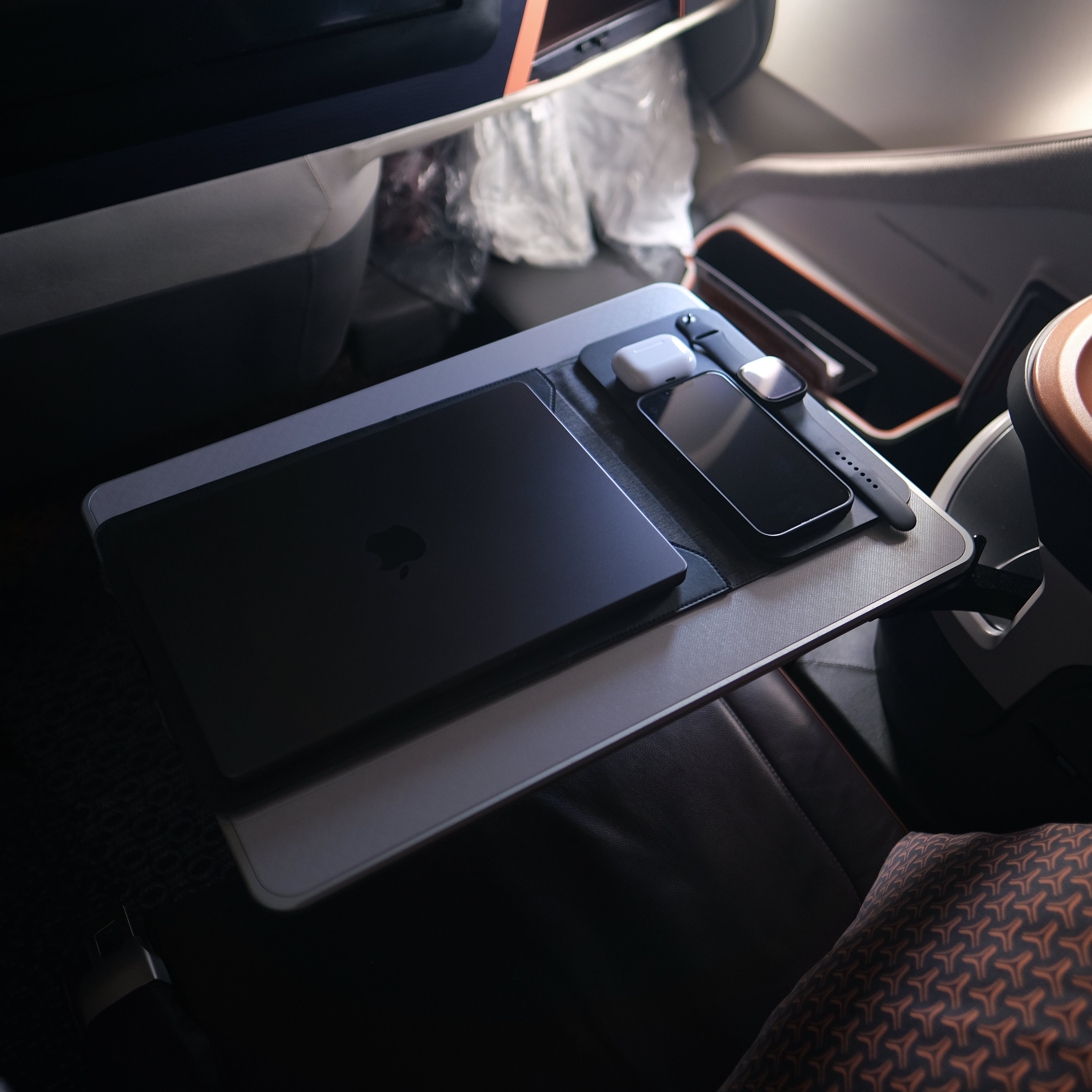 NODE. Minimalist Black Laptop Sleeve with Apple Magsafe compatible charging docks for iPhone, Airpods and Apple Watch. on a tray table in an Business Class Singapore Airlines airplane. 