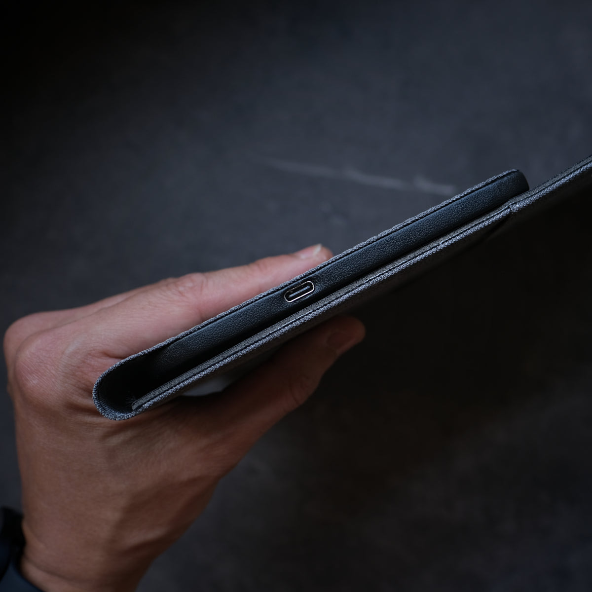 Hand holding a black leather wallet against a dark background. NODE. Minimalist Black Laptop Sleeve with Apple Magsafe compatible charging docks for iPhone, Airpods and Apple Watch.