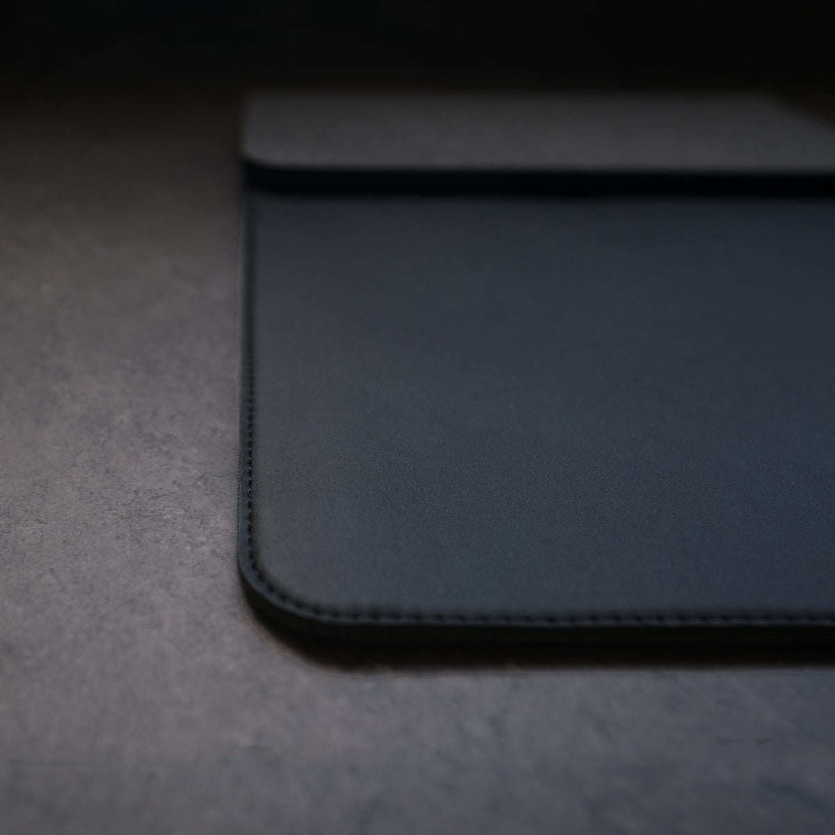 Black leather wallet on a dark textured surface. NODE. Minimalist Black Laptop Sleeve with Apple Magsafe compatible charging docks for iPhone, Airpods and Apple Watch.